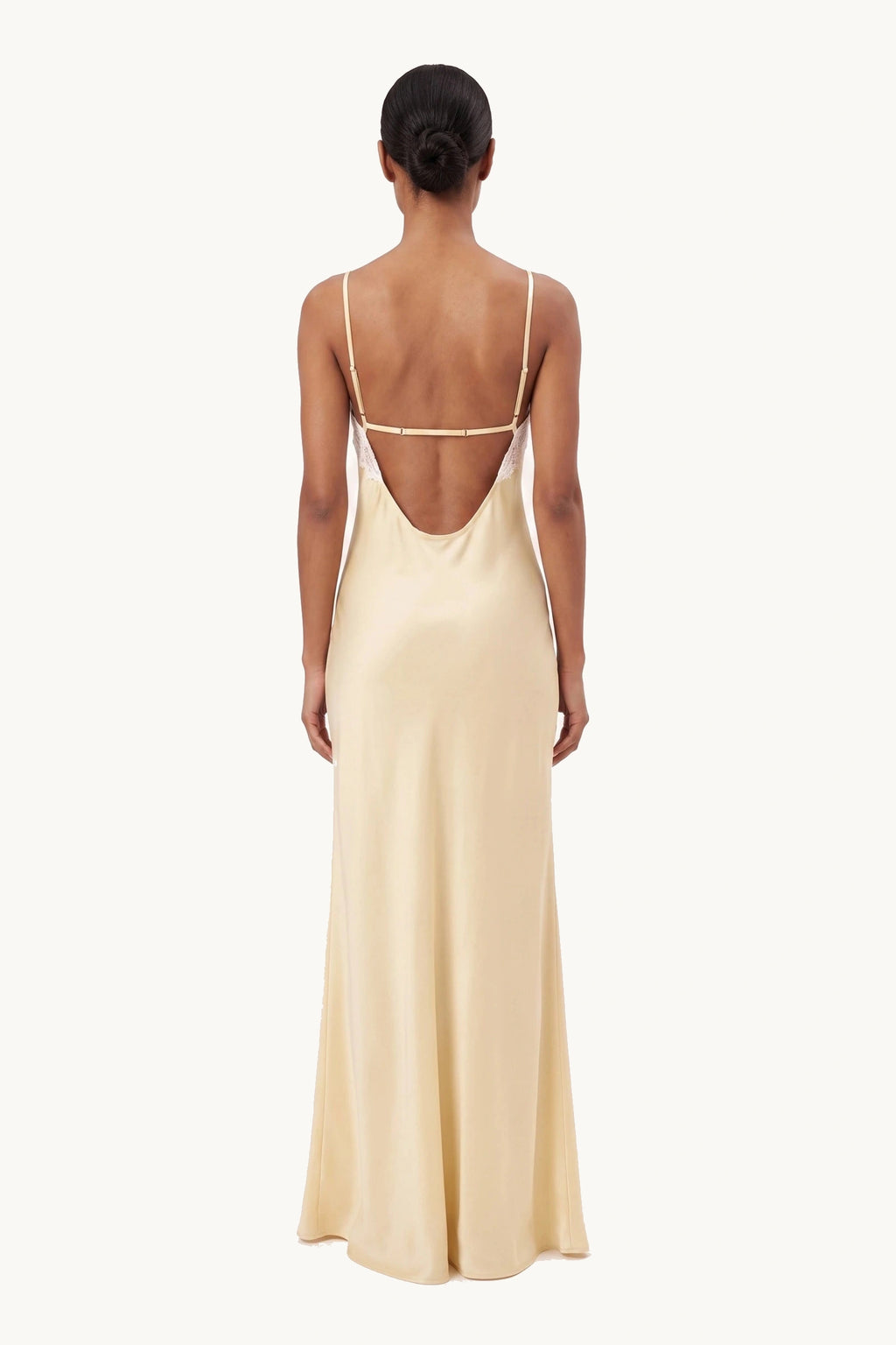 Robe satin dentelle dos nu Alyssa jaune portée de dos par une mannequin métisse sur fond neutre clair, dos nu à fines bretelles et satin fluide