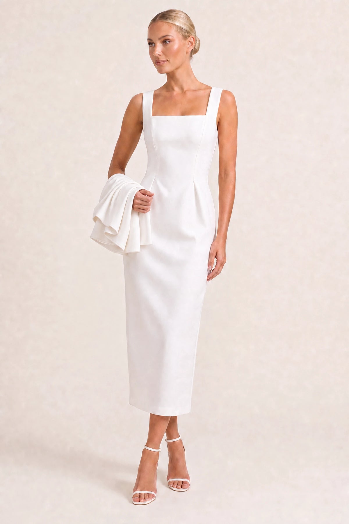 Robe tailleur Alice blanche sans cape portée par la mannequin Chloé sur fond beige ivoire fond neutre clair, bretelles larges, encolure carrée, plis structurés à la taille et petite cape blanche pliée sur le bras.