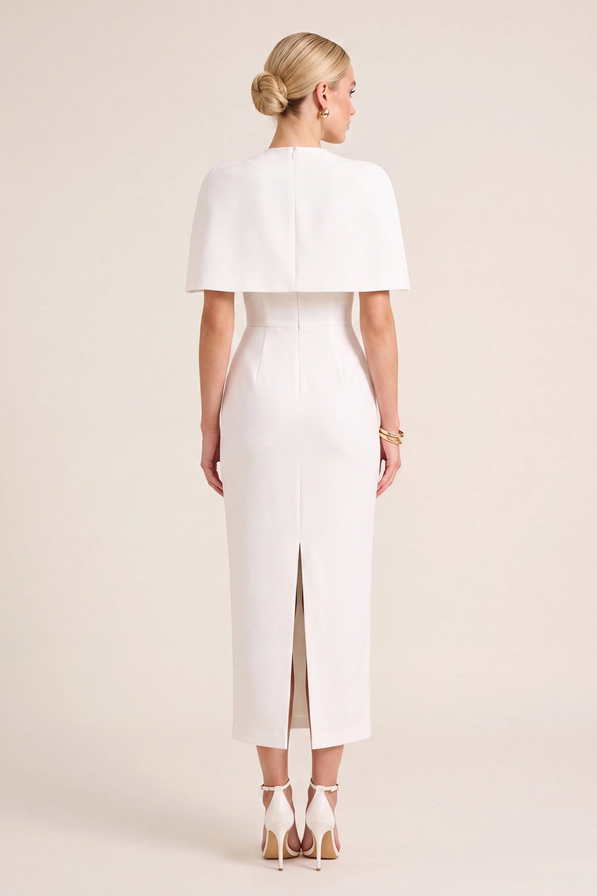 Robe tailleur Alice blanche vue de dos sur mannequin Chloé, cape structurée couvrant les épaules, coupe midi ajustée et fente arrière visible sur fond neutre clair pour présenter les détails de finition.