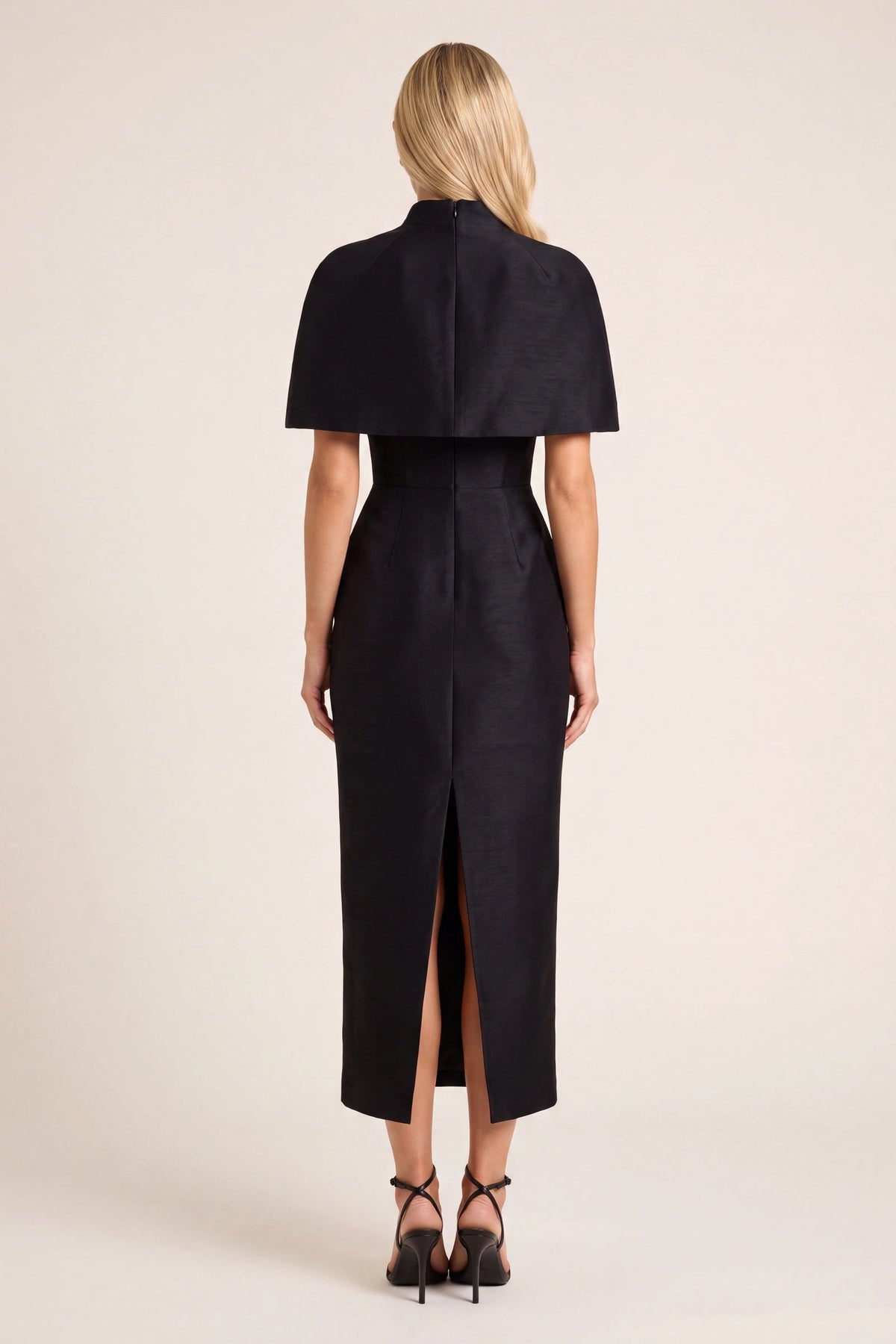 Robe tailleur Alice noire vue de dos sur mannequin Chloé, cape élégante, coupe midi structurée et fente arrière nette sur fond beige ivoire fond neutre clair, idéale pour visualiser la silhouette complète.