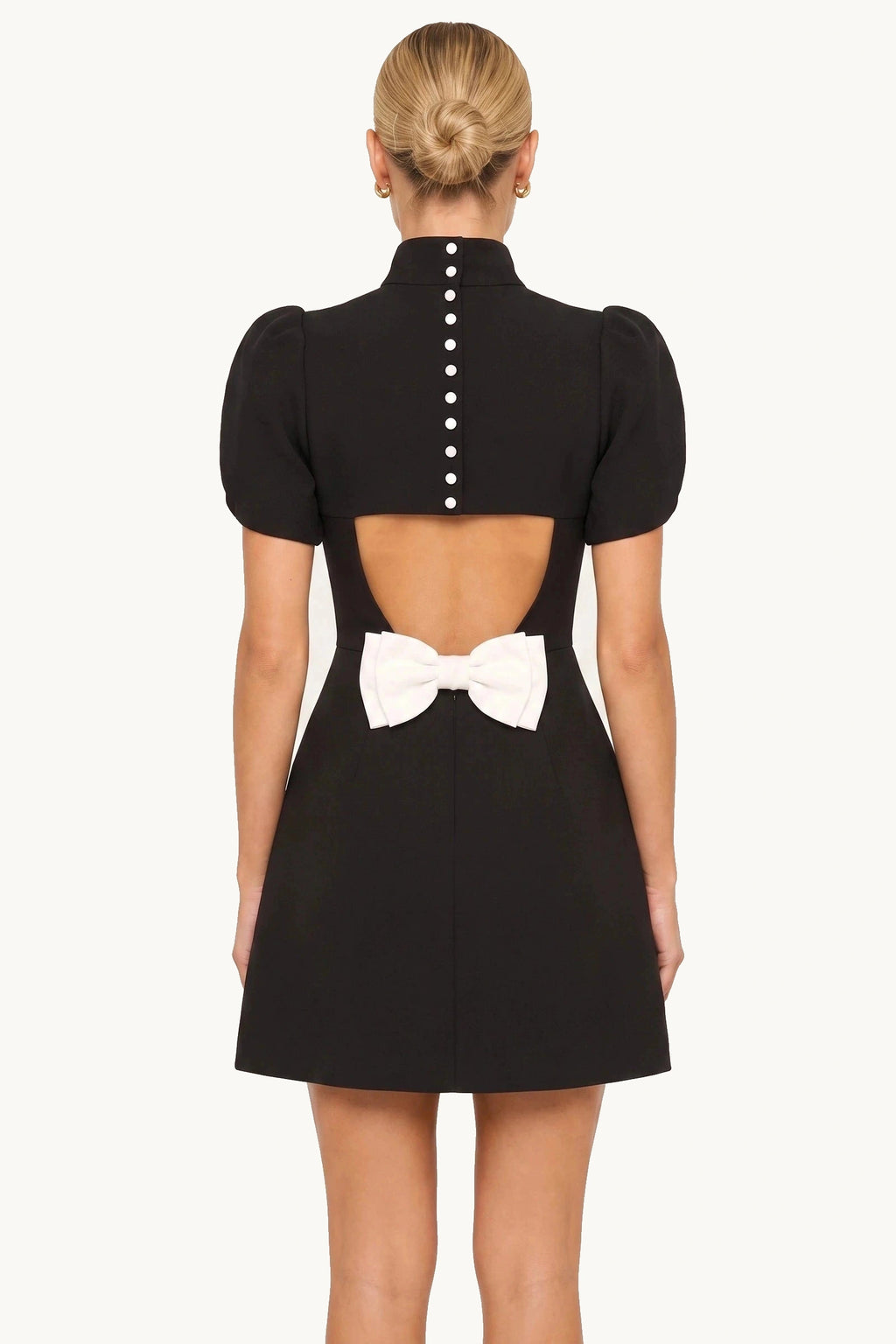Robe tailleur courte Élise noire portée de dos par le mannequin Chloé sur fond neutre clair, dos ajouré avec boutons et nœud contrasté