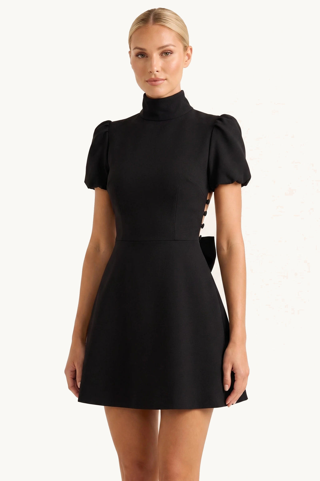 Robe tailleur courte Élise noire portée de face par le mannequin Chloé sur fond neutre clair, effet tailleur chic, col montant et coupe courte structurée