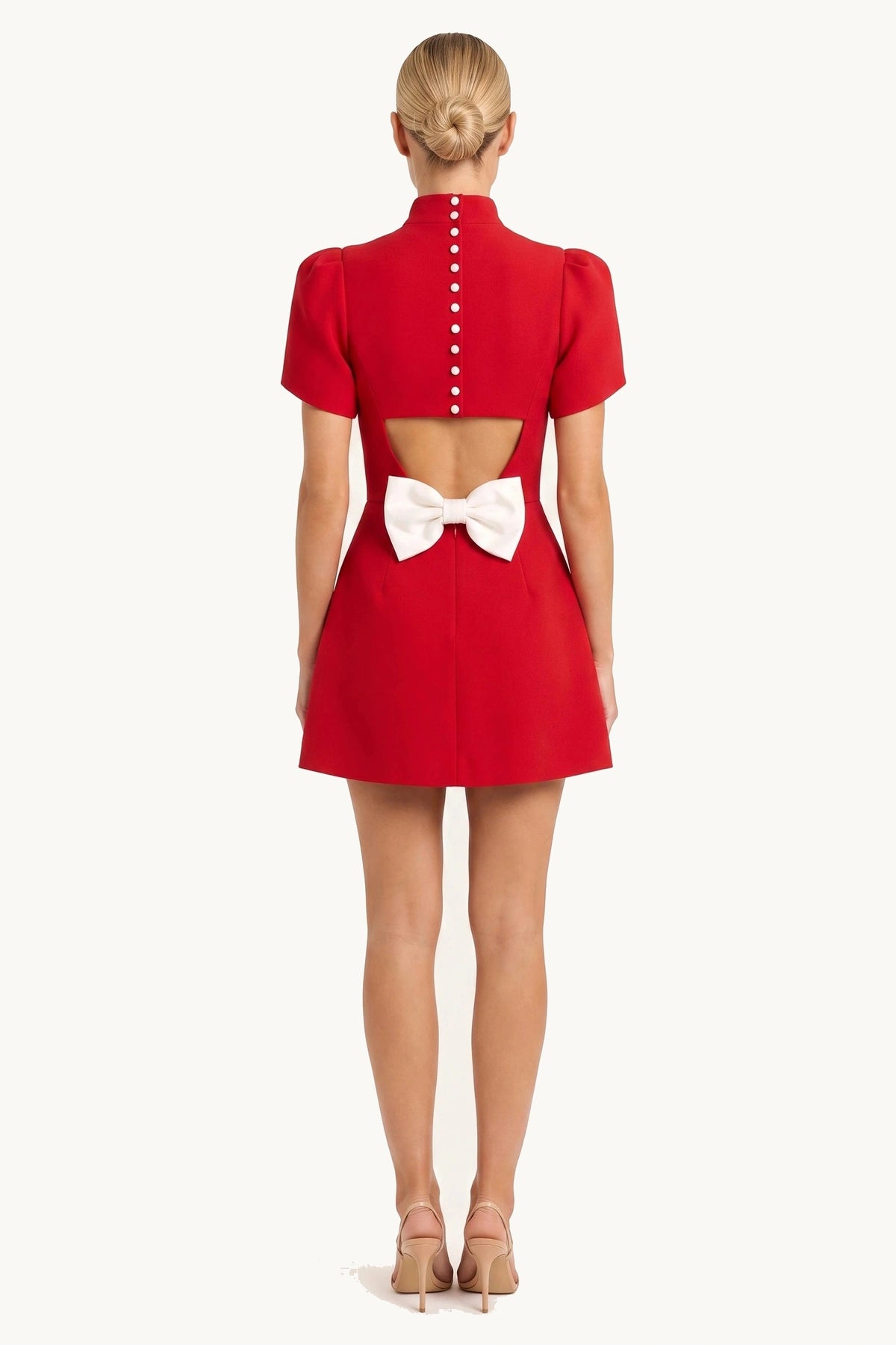 Robe tailleur courte Élise rouge portée de dos par le mannequin Chloé sur fond neutre clair, dos ouvert avec boutons et grand nœud signature