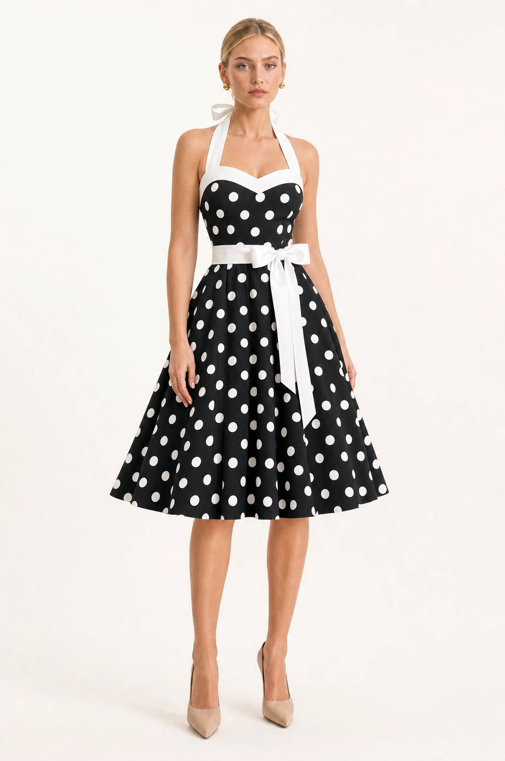 Robe Année 50 noire à pois Amélie portée de face par Sophie cheveux blonds tirés en chignon, encolure halter nouée à la nuque, bustier en cœur bordé de blanc, ceinture blanche nouée en nœud papillon, jupe en corolle ample longueur genou