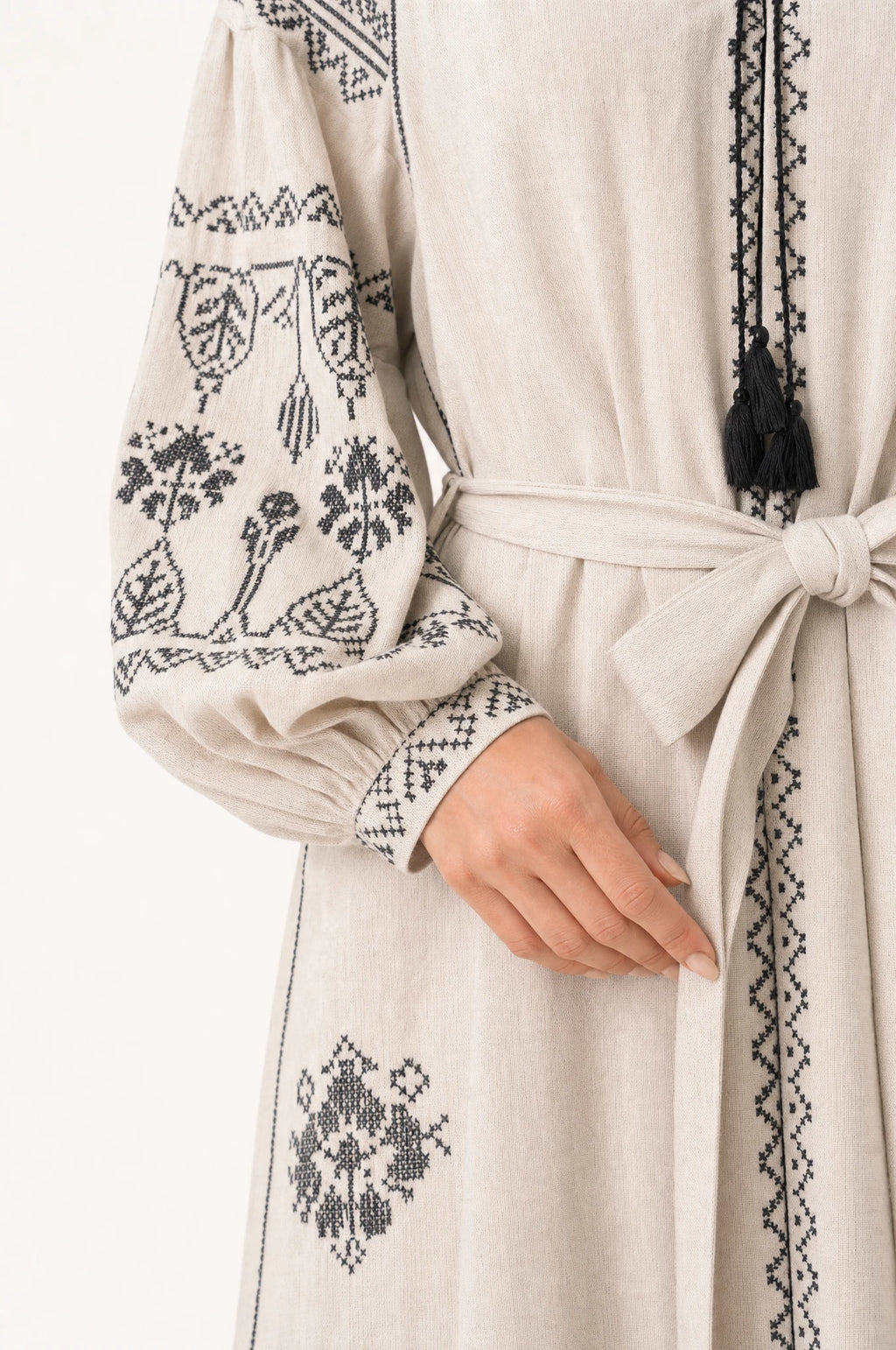 Gros plan sur la broderie ethnique noire et la ceinture nouée de la robe vintage beige Elsa, détail des manches bouffantes resserrées et du tissu coton lin