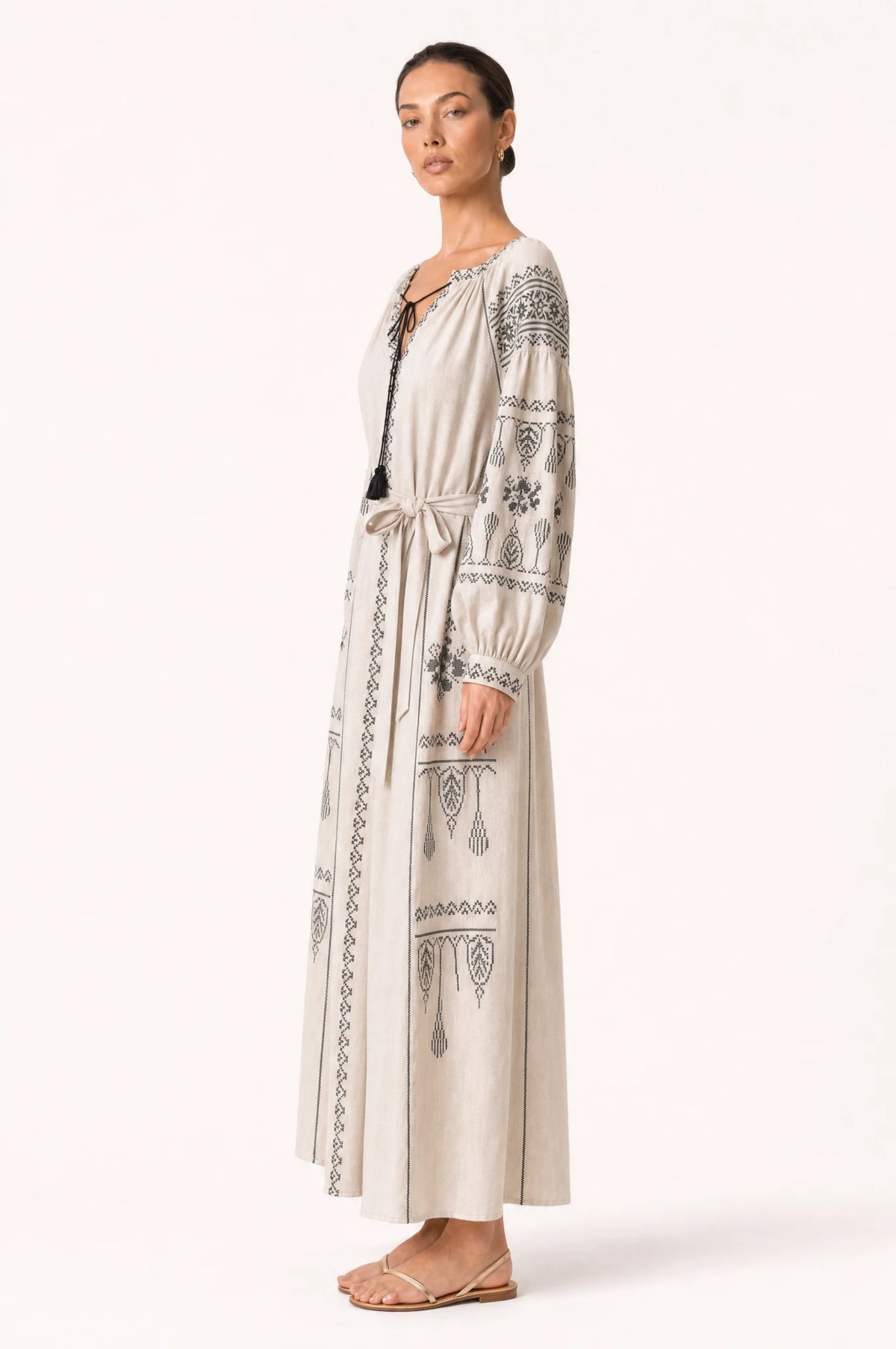 Robe vintage brodée beige Elsa vue de profil portée par Nath, silhouette évasée coupe empire, broderie ethnique noire, jupe longue jusqu'aux chevilles, ceinture nouée à la taille
