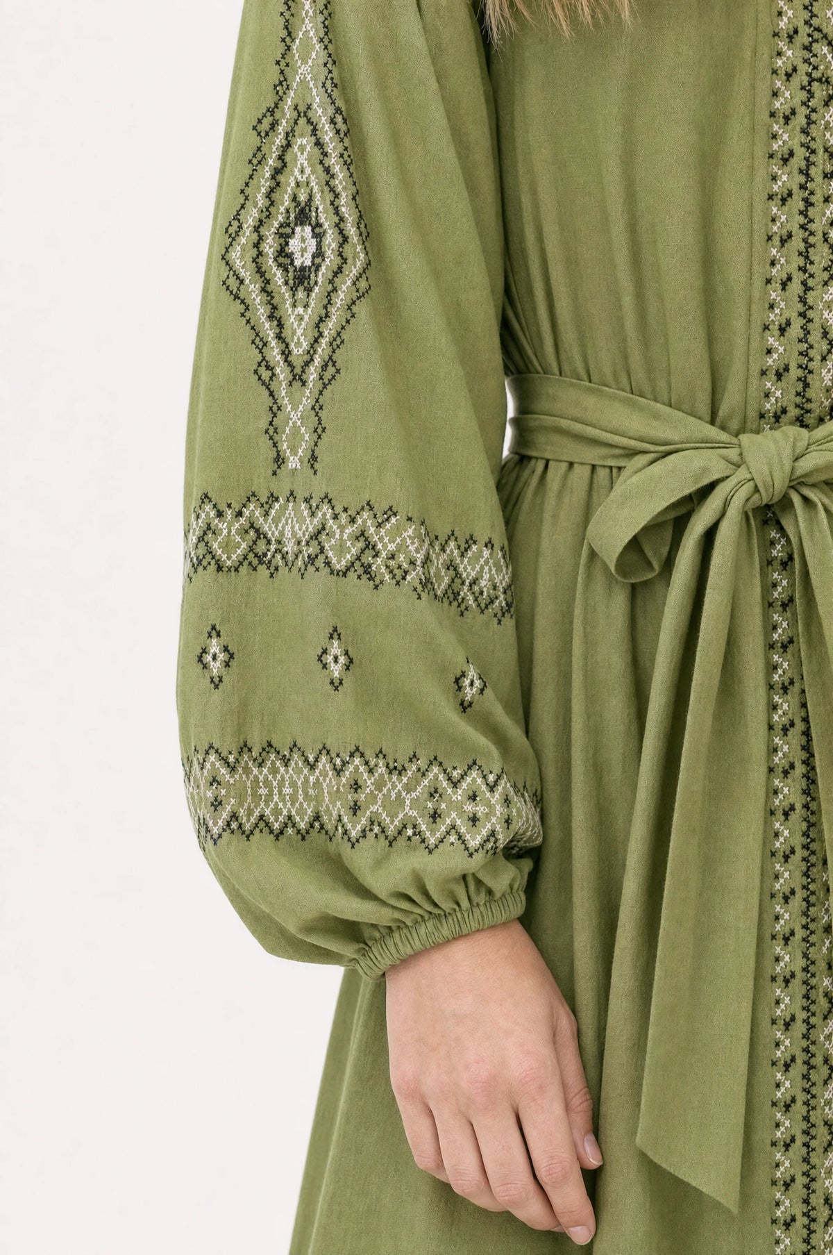 Gros plan sur la broderie ethnique bicolore noir et blanc et la ceinture nouée de la robe vintage verte Romane, détail des manches bouffantes resserrées et du tissu coton lin