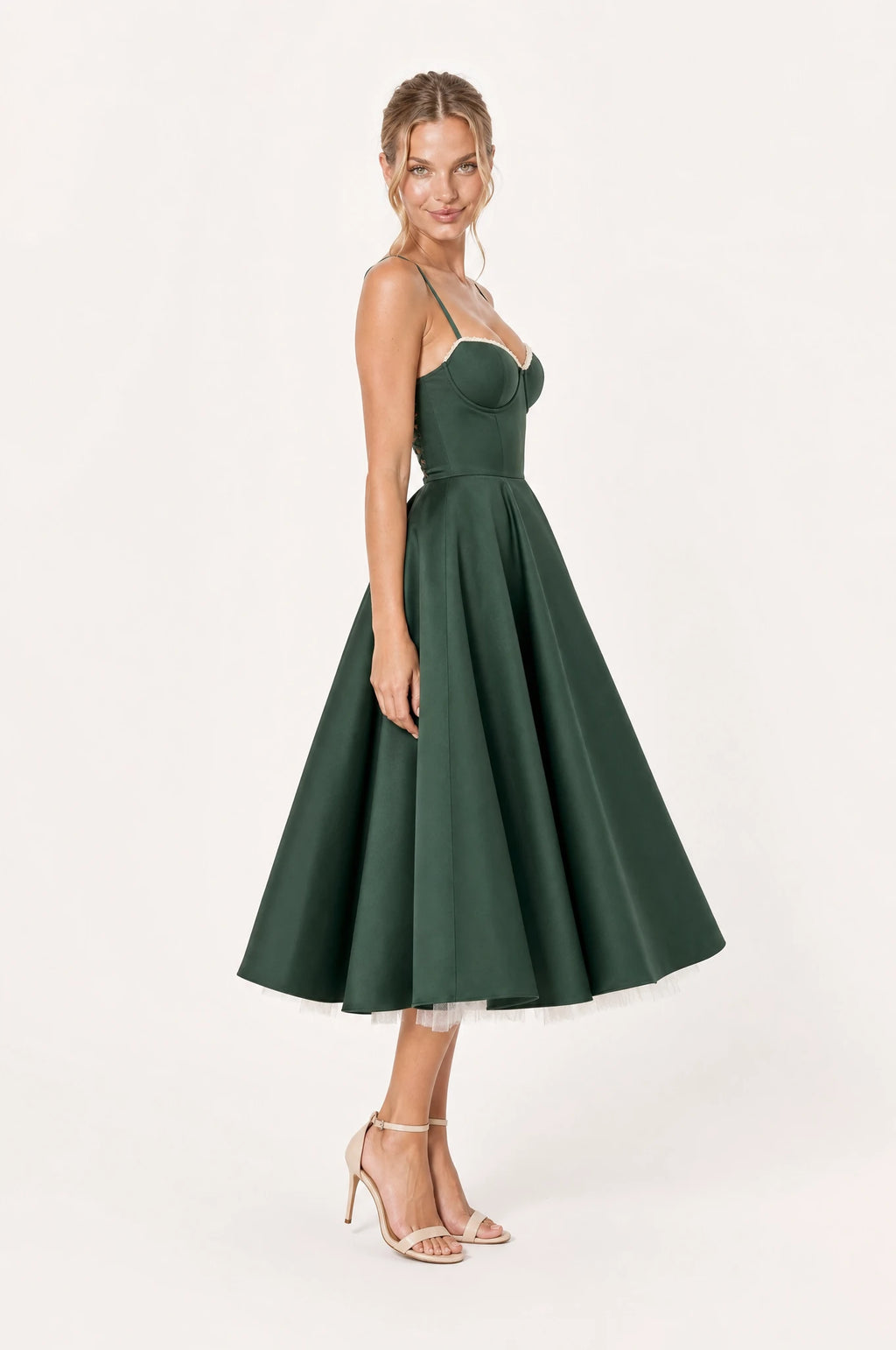 Robe vintage bustier vert émeraude Éléonore vue de profil portée par Aude, taille cintrée, jupe en corolle ample avec jupon ivoire dépassant sous l'ourlet