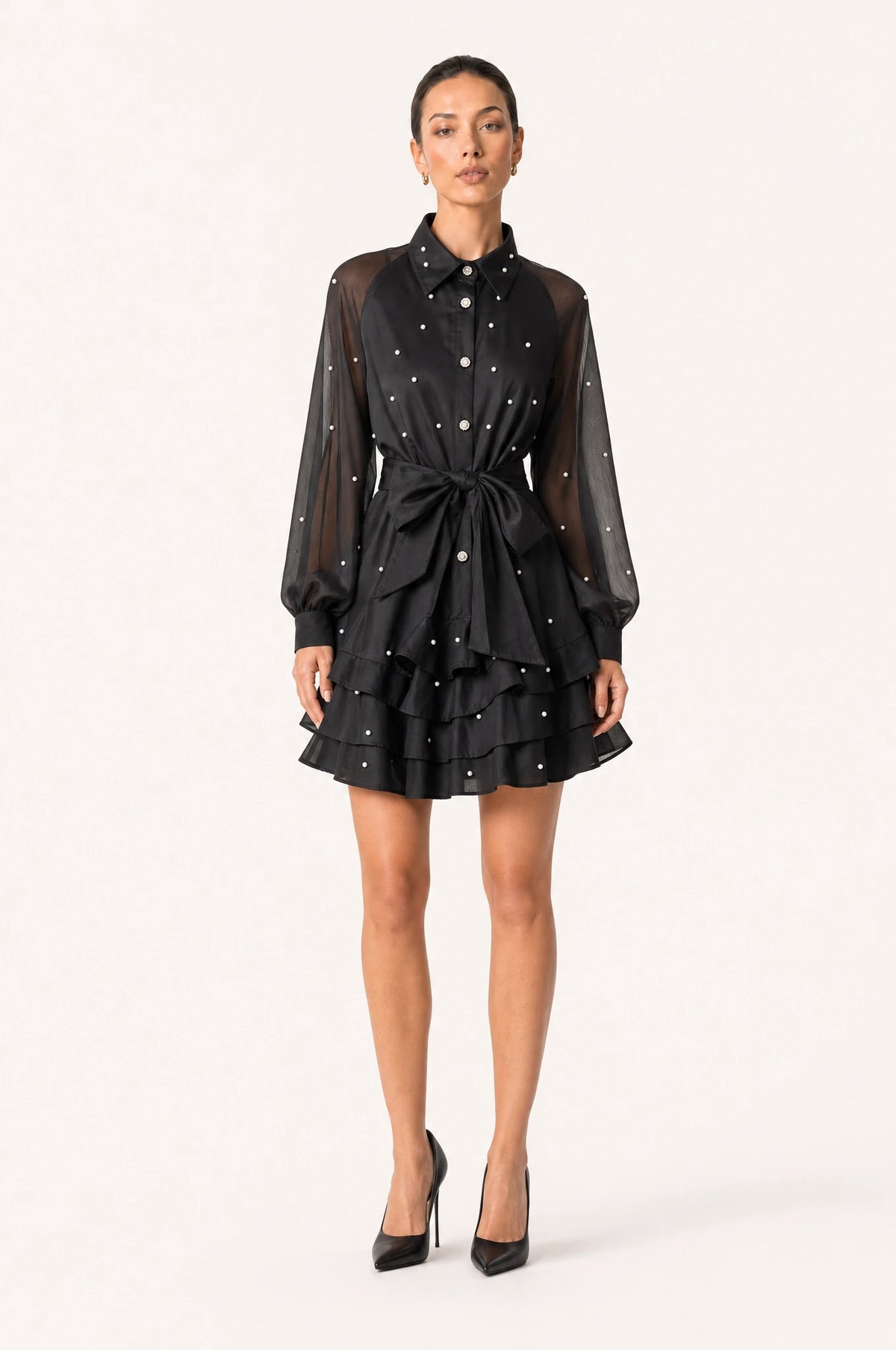 Robe vintage perlée noire Héloïse portée de face par Nath chignon sleek, col chemisier structuré, boutons perlés et strass sur le buste, manches bouffantes en organza semi-transparent, ceinture nouée à la taille, jupe courte à volants superposés