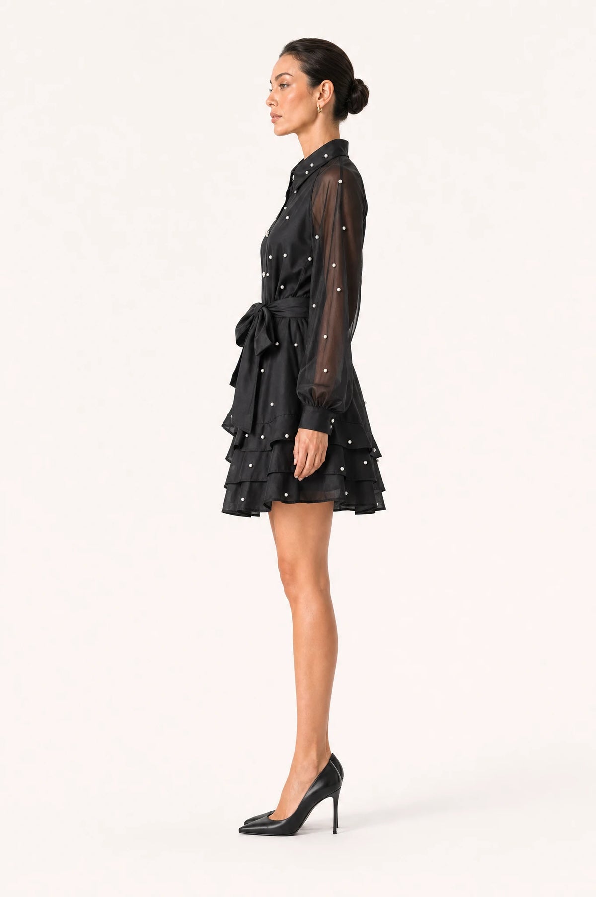 Robe vintage perlée noire Héloïse vue de profil portée par Nath, silhouette évasée coupe patineuse, manches longues en organza transparent, jupe à volants superposés jusqu'au genou