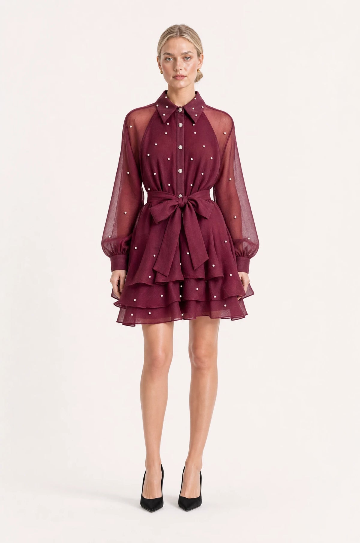 Robe vintage perlée rouge grenat Garance portée de face par Sophie chignon sleek, col chemisier structuré, boutons perlés et strass sur le buste, manches bouffantes en organza semi-transparent, ceinture nouée à la taille, jupe courte à volants superposés