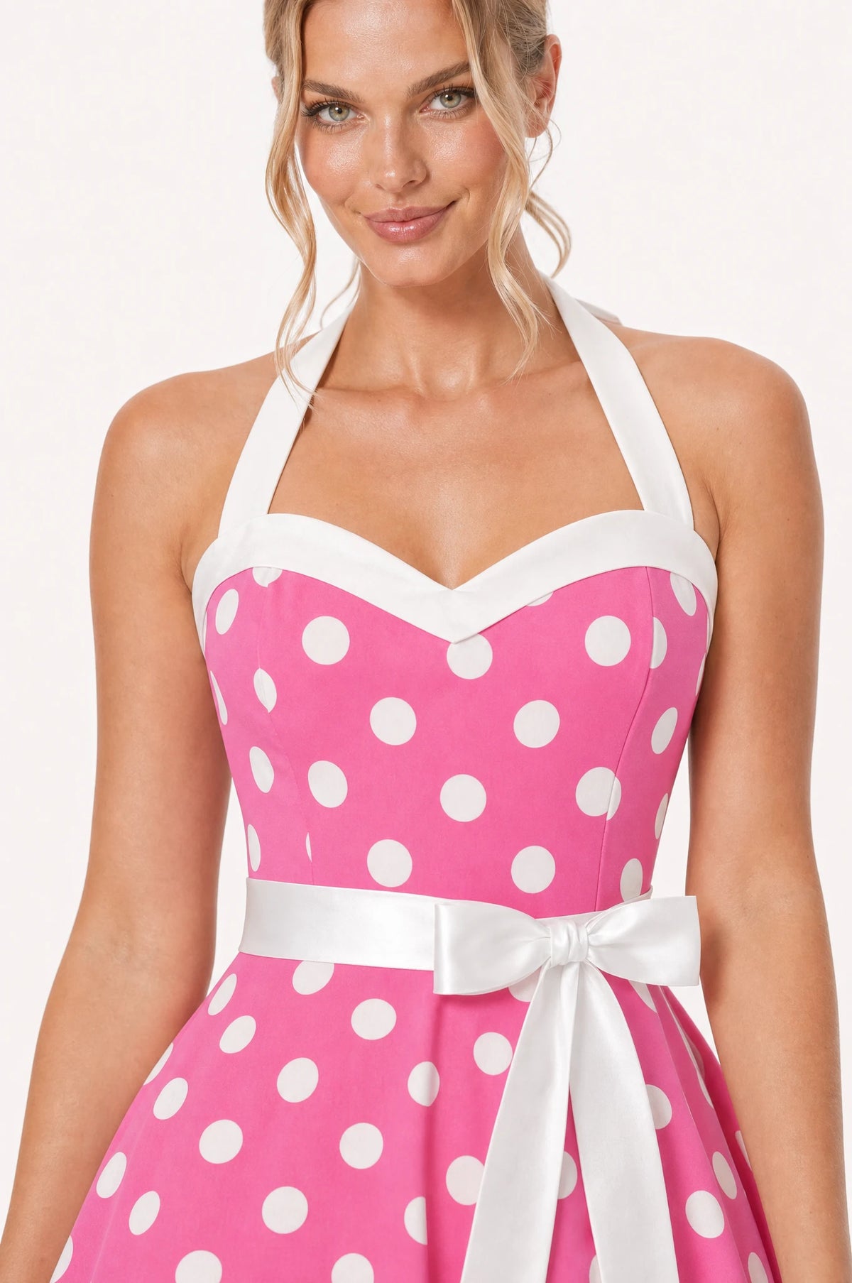Gros plan sur le col halter, le bustier en cœur bordé de blanc et le nœud à la ceinture de la robe Année 50 rose à pois Simone, détail de l'imprimé pois blancs