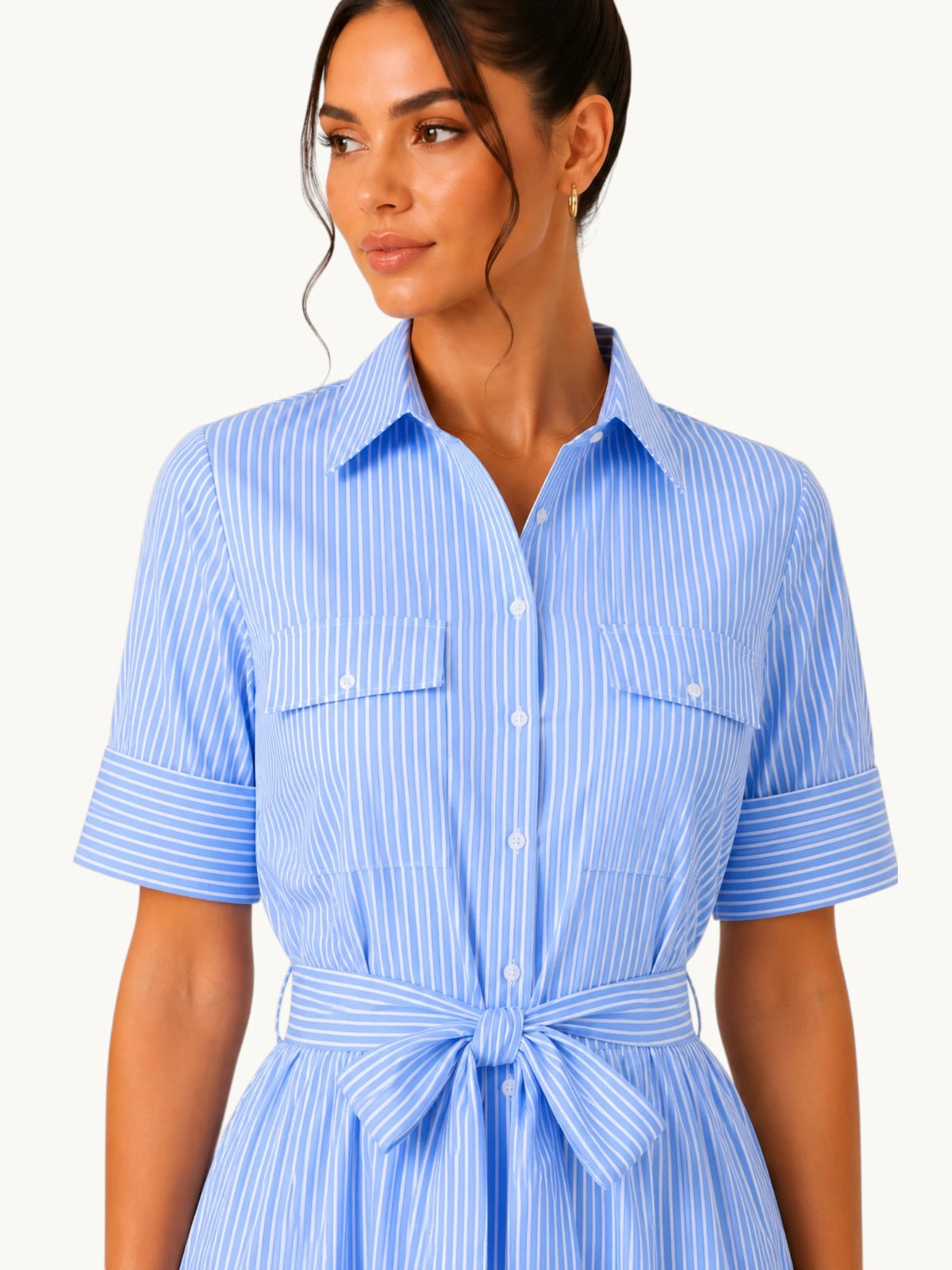 Détail de la robe chemise bleu ciel rayée avec poches poitrine, col chemisier, boutons ton sur ton et ceinture nouée soulignant élégamment la taille.