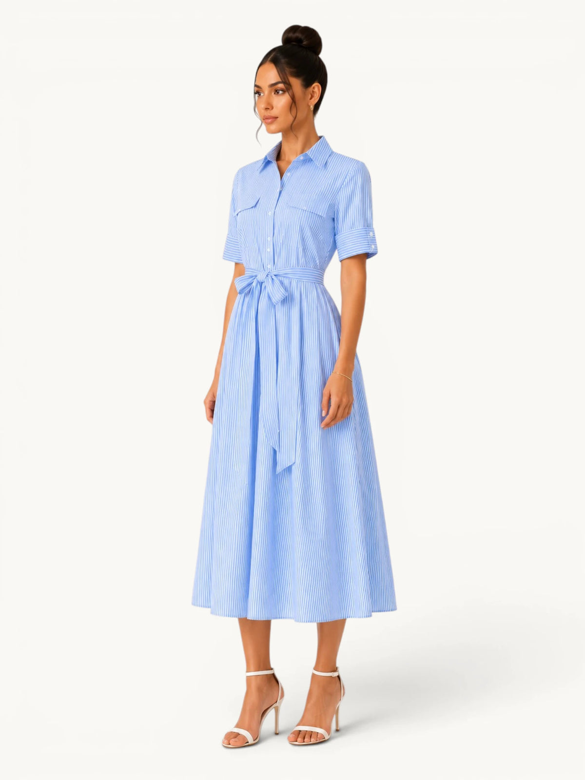 Robe chemise rayée bleu ciel pour femme avec col classique, ceinture assortie et coupe midi élégante, portée en angle trois-quarts pour mettre en valeur sa silhouette structurée.