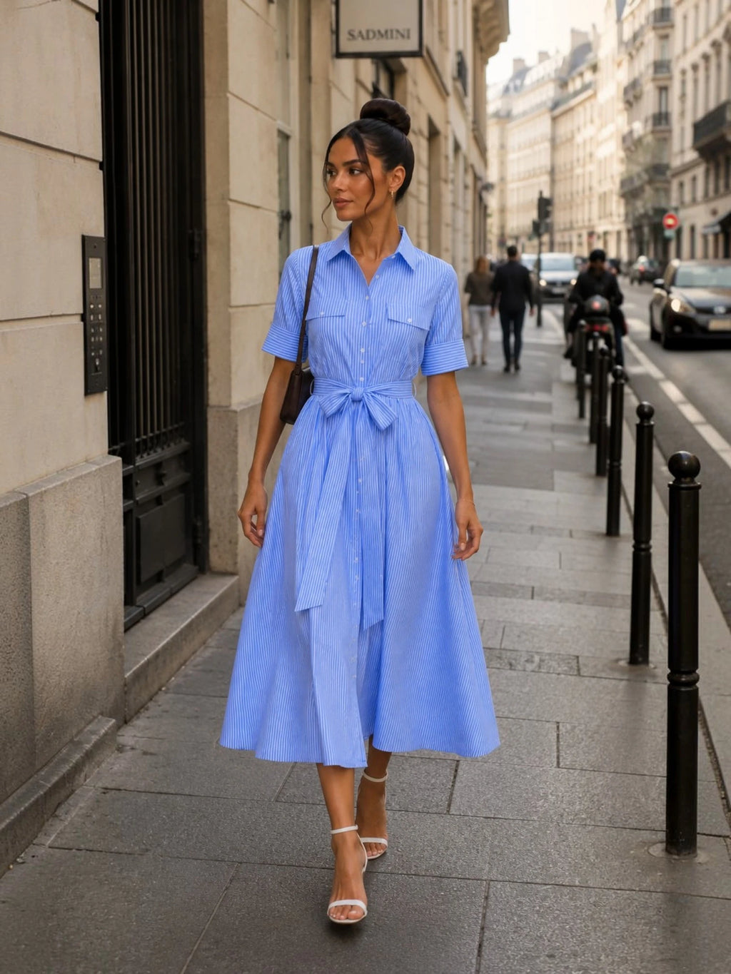 Robe chemise midi bleu clair rayée avec ceinture nouée portée dans une rue parisienne, idéale pour un look chic urbain, féminin et moderne au quotidien.