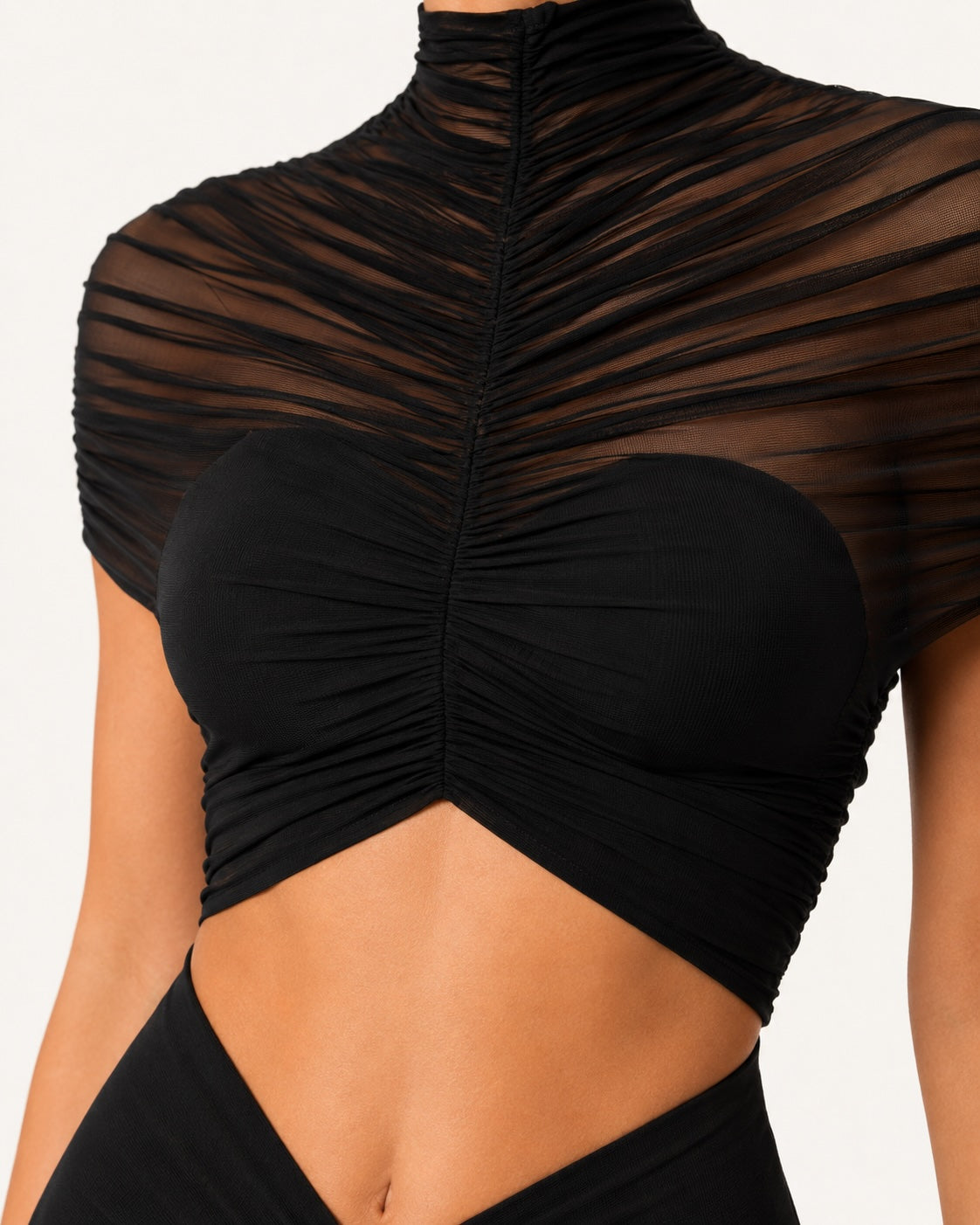Gros plan sur le bustier drapé en tulle transparent d’une robe de soirée noire glamour, avec col montant et découpe sous la poitrine pour une silhouette sophistiquée.