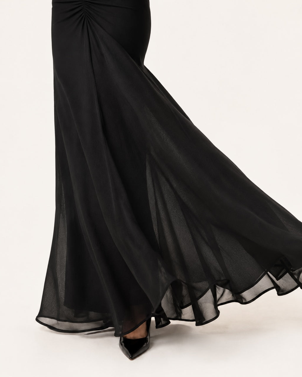 Détail du bas de robe de soirée noire longue à coupe sirène, confectionnée en voile fluide et léger, offrant un mouvement élégant et aérien à chaque pas.