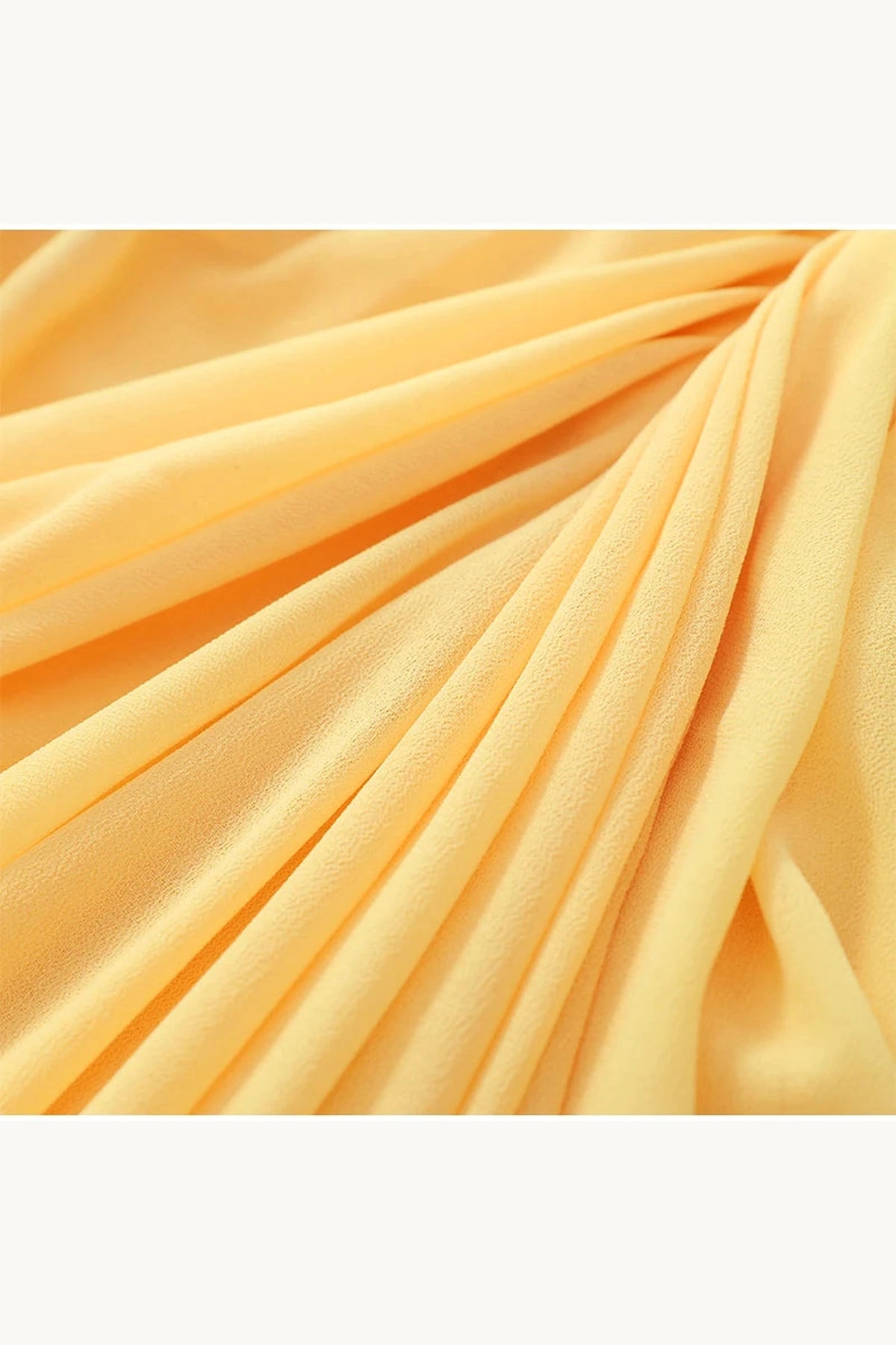 Morceau du tissu drapé de la robe élégante jaune pastel, mettant en avant sa fluidité et sa légèreté.