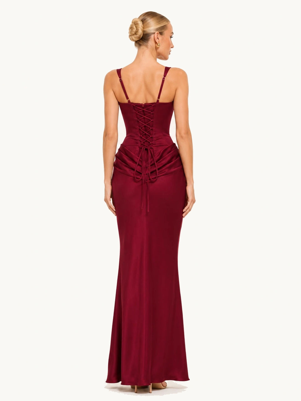 La femme blonde est de dos, la robe est longue de couleur bordeaux. Elle a un lacet dans le dos qui lui permet de pouvoir ajuster la taille tout en apportant beaucoup de raffinement à cette belle robe.