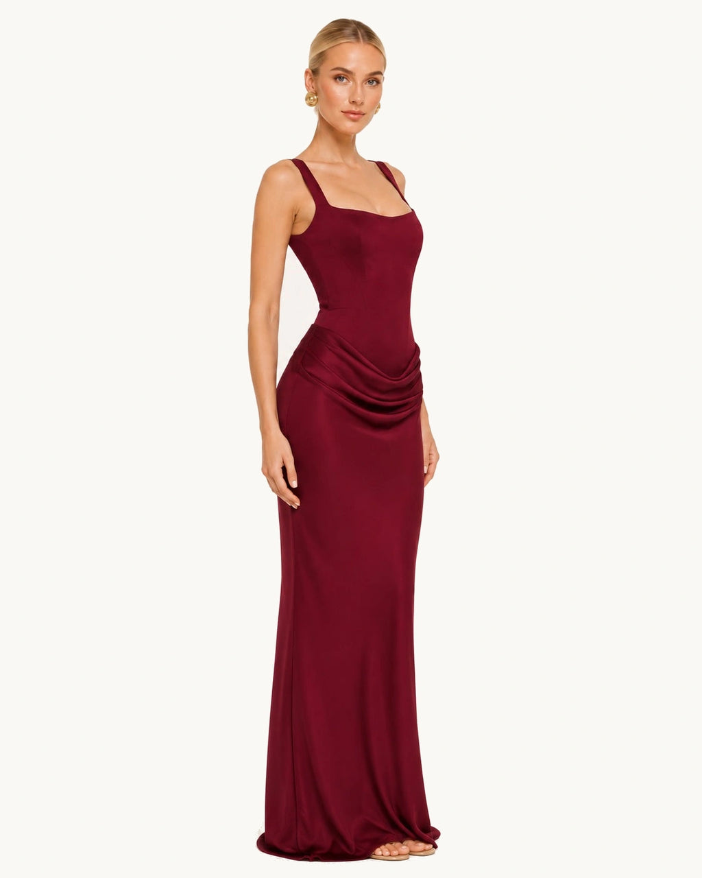 Robe bordeaux longue avec un joli drapé au niveau de la taille. Vue de profile, le haut de la robe avec des bretelles et son col carré légèrement décolleté met en valeur le port de tête.