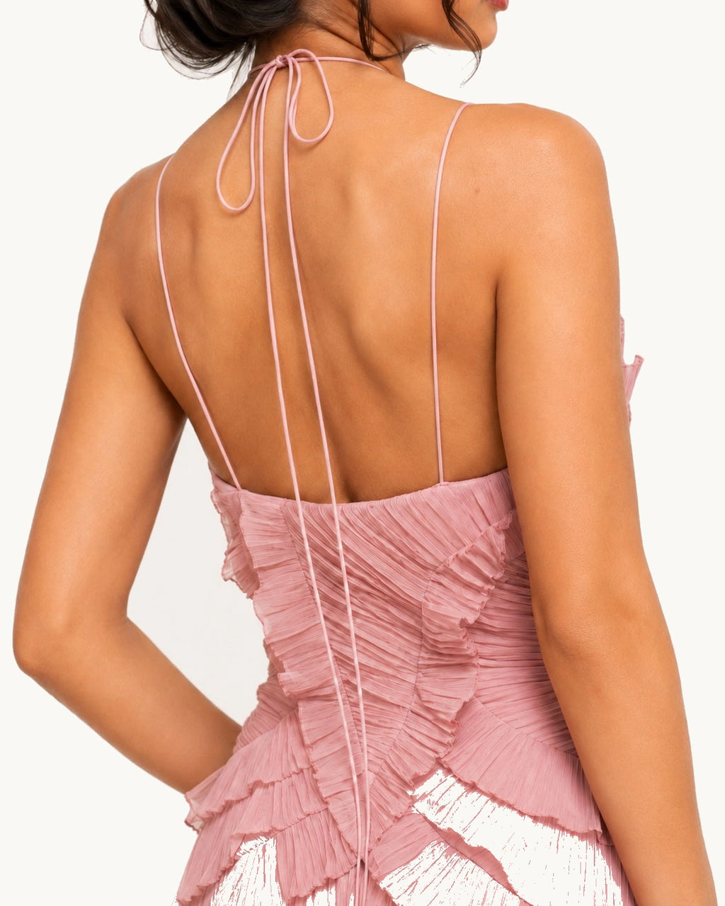 Vue arrière d'une robe longue rose poudré à fines bretelles et dos dégagé, soulignant la silhouette féminine avec des détails plissés raffinés.