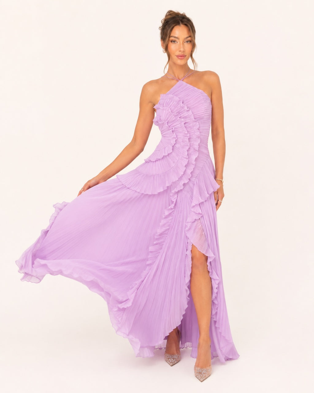 Robe longue plissée lilas avec volants en cascade et fente élégante, portée en mouvement pour mettre en valeur la fluidité de la jupe.