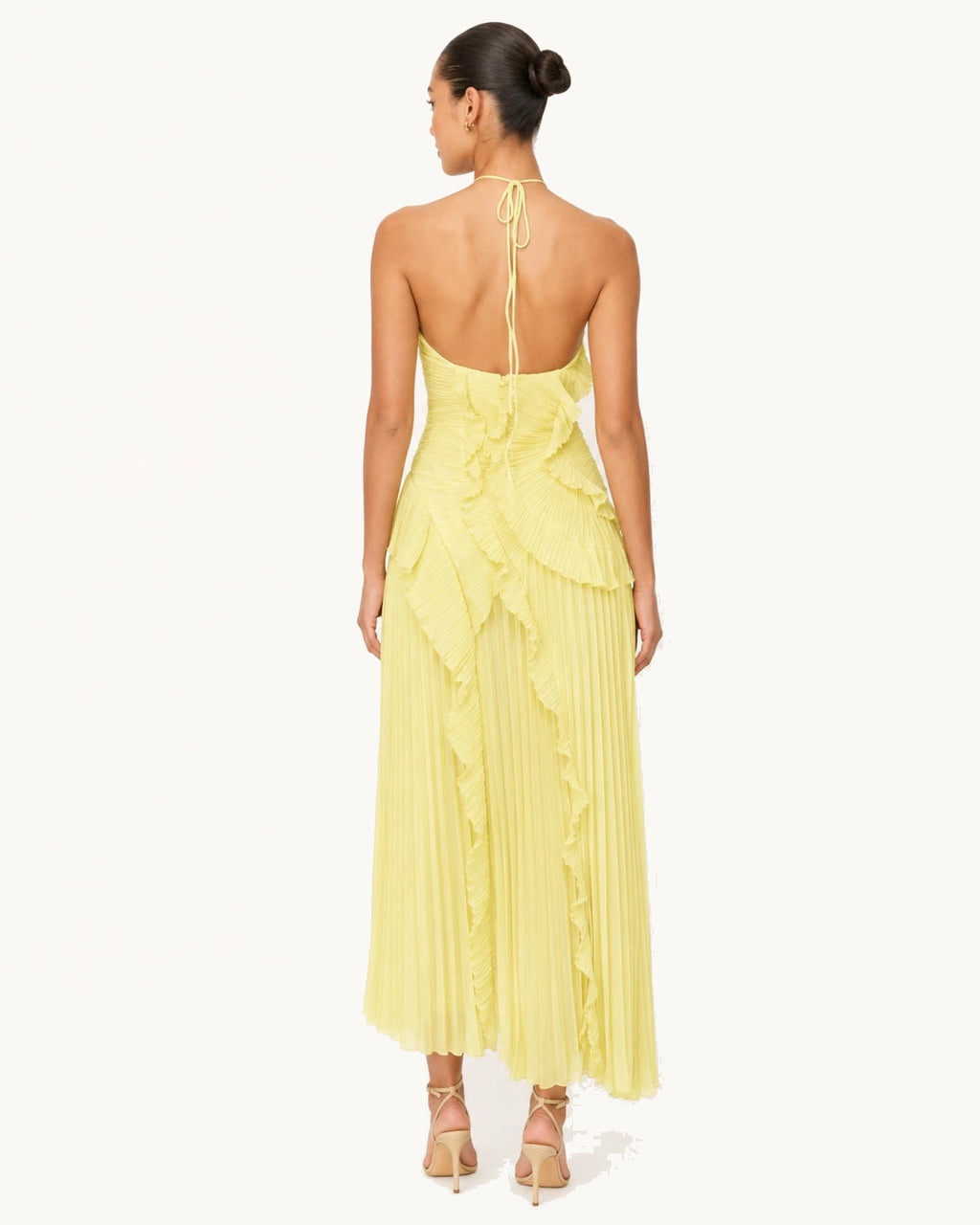 Dos nu élégant avec lien tour de cou sur robe longue jaune plissée, mettant en valeur les épaules et le dos pour une allure sophistiquée lors d’une cérémonie.